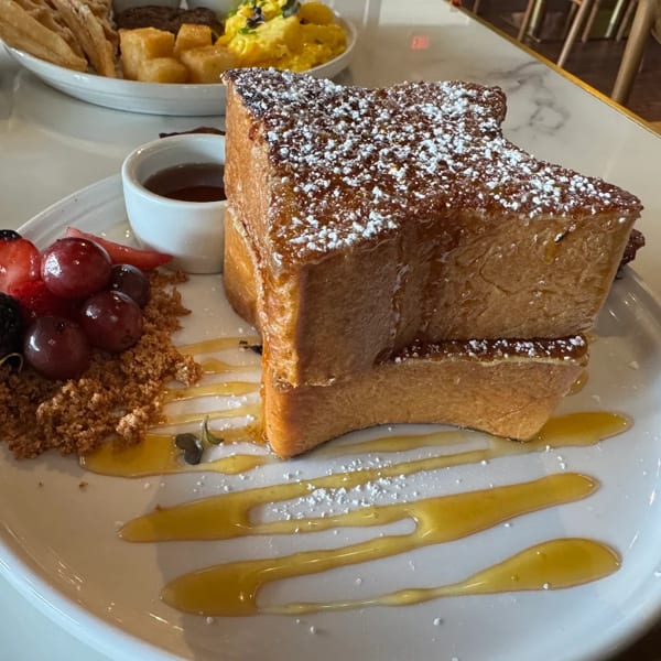Thick-cut French toast with powdered sugar, berries, granola, and syrup on a white plate.