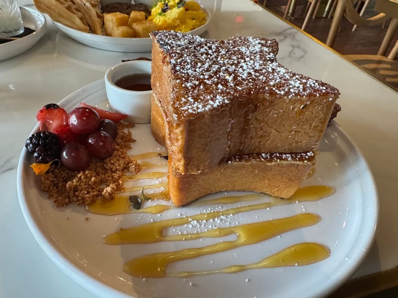 Thick-cut French toast with powdered sugar, berries, granola, and syrup on a white plate.