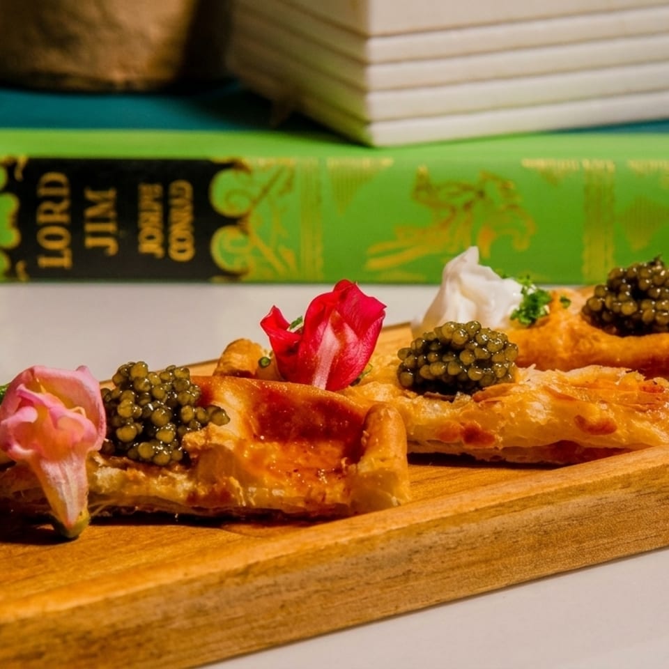 Puff pastry appetizers topped with caviar, cream, and edible flowers on a wooden board.