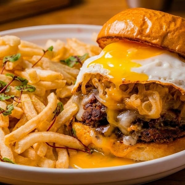 Gourmet burger with a fried egg, caramelized onions, melted cheese, and a side of french fries.