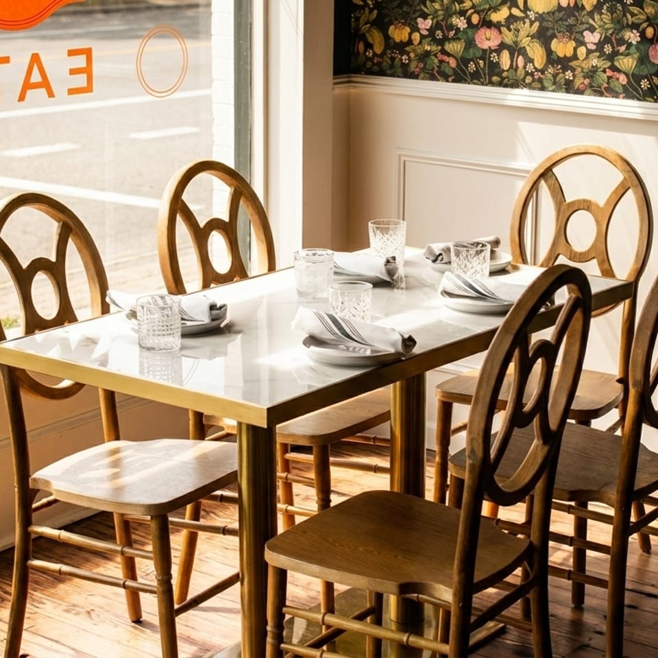 A sunlit restaurant dining table set with plates, glasses, and napkins, next to a window.