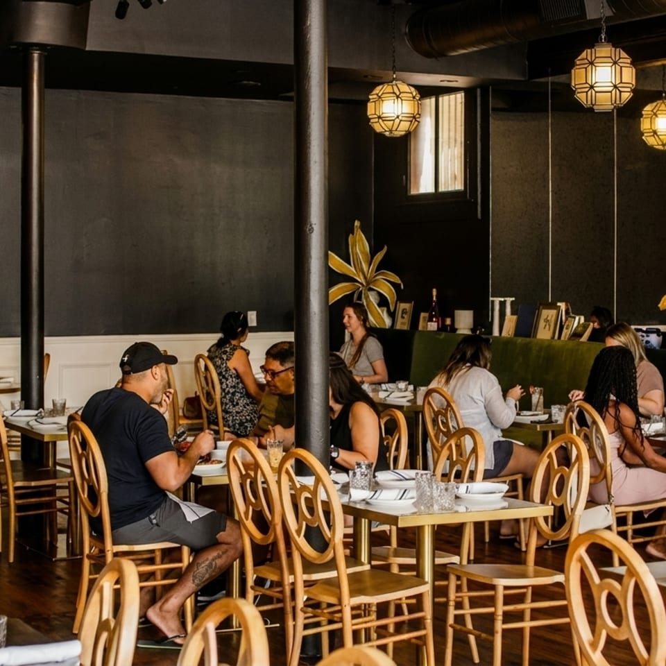 Diners seated at tables in a restaurant with dark walls, green banquettes, and ornate light fixtures.
